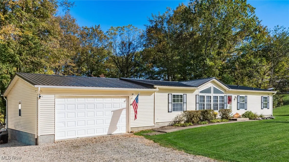 View of front facade with gravel driveway, a front lawn, a metal roof, and a garage