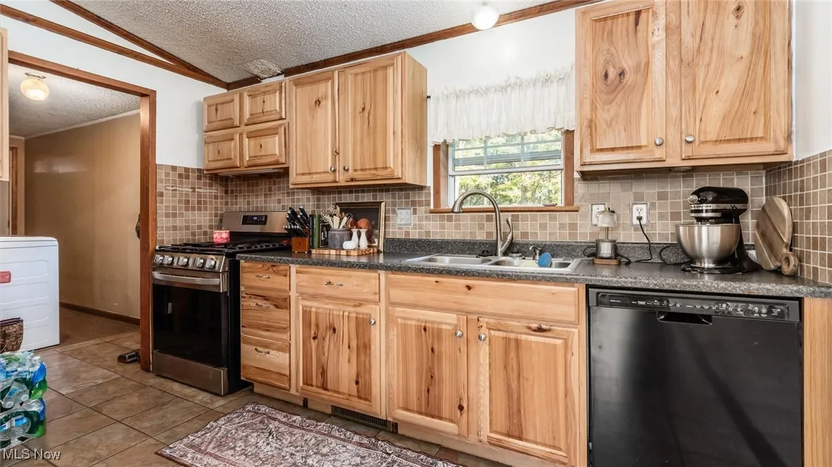 Kitchen featuring a textured ceiling, black dishwasher, stainless steel gas range, dark countertops, and decorative backsplash