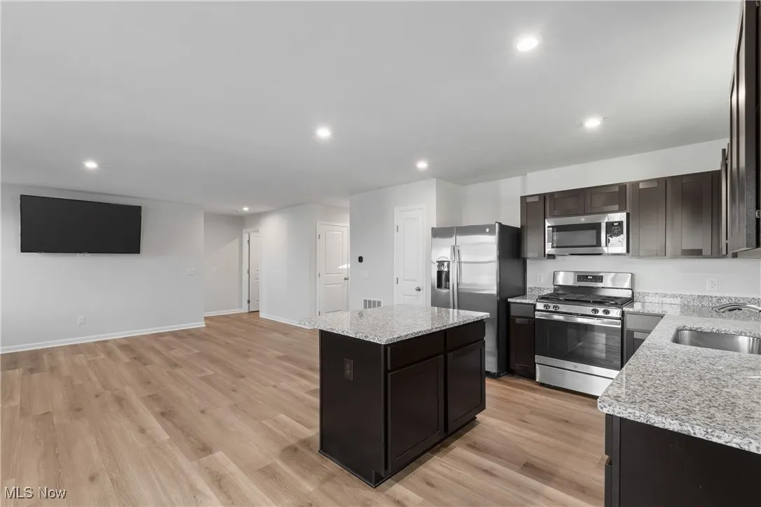 Kitchen featuring appliances with stainless steel finishes, recessed lighting, light wood finished floors, light stone counters, and a kitchen island
