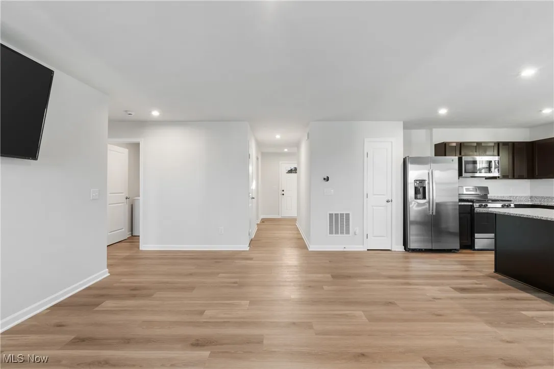 Kitchen with stainless steel appliances, recessed lighting, light wood-style floors, open floor plan, and light stone countertops