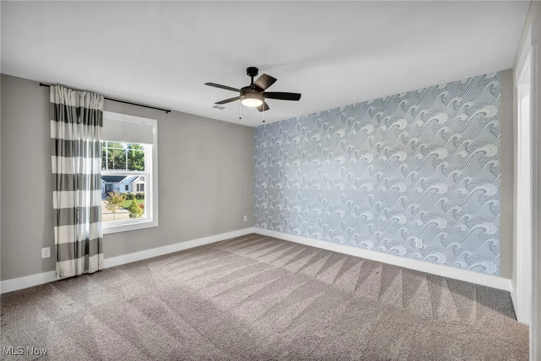 Unfurnished room featuring wallpapered walls, carpet flooring, an accent wall, and ceiling fan