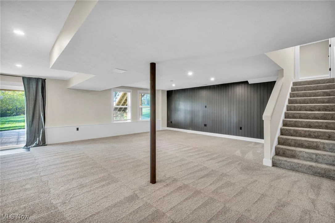 Basement featuring light carpet, wood walls, stairway, and recessed lighting