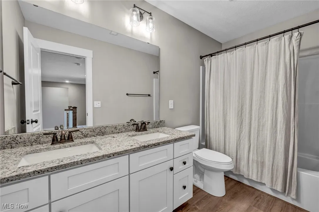Full bath featuring shower / bath combo with shower curtain, dark wood-style floors, and double vanity