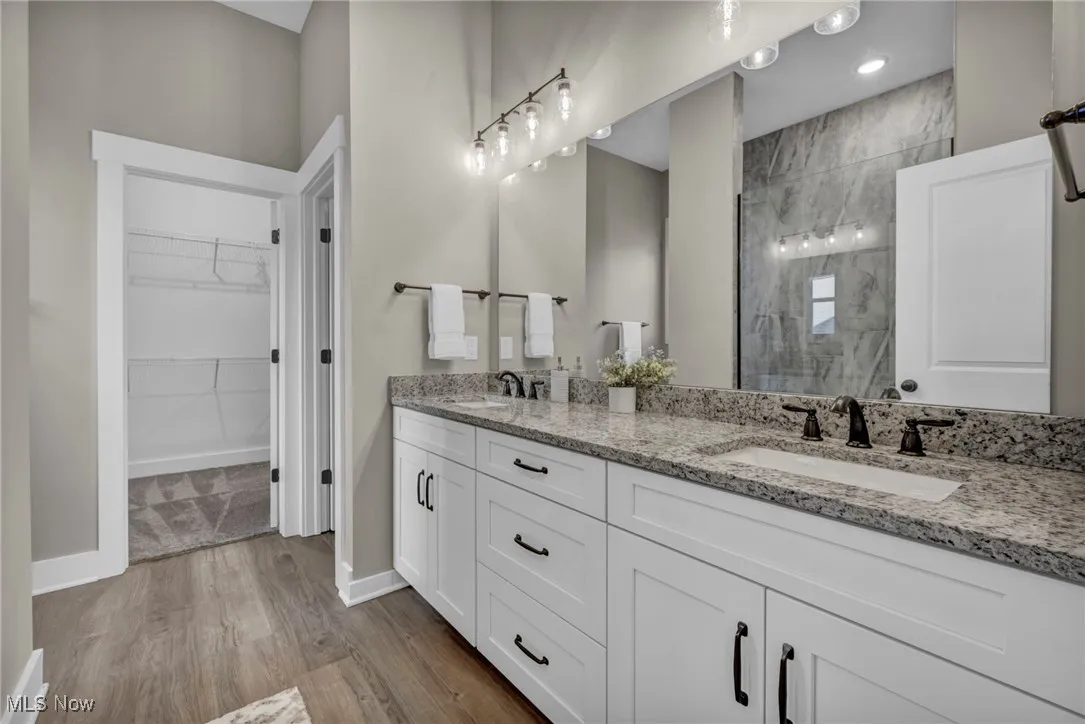 Full bath with a marble finish shower, double vanity, dark wood-style flooring, and a walk in closet