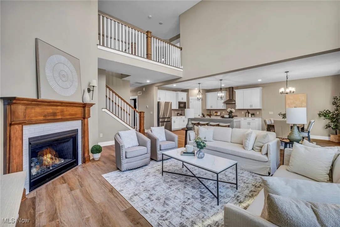 Living room featuring light wood-type flooring, a chandelier, a glass covered fireplace, a towering ceiling, and stairway