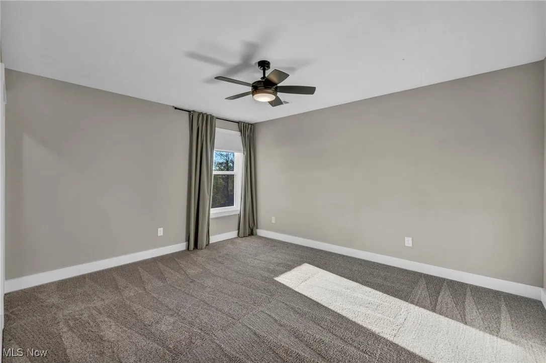 Carpeted empty room with baseboards and a ceiling fan