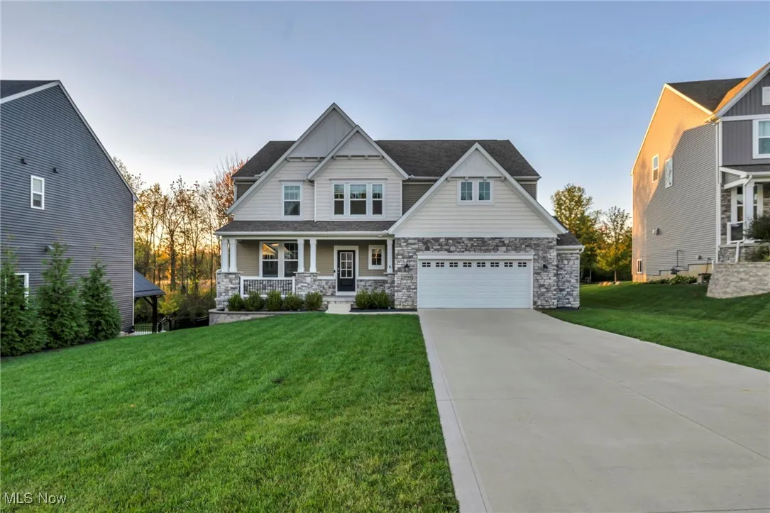 Craftsman inspired home featuring a porch, a yard, driveway, and stone siding