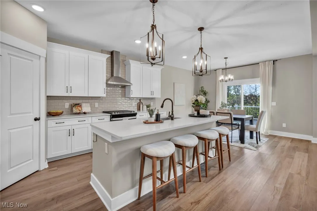 Kitchen featuring a kitchen bar, decorative backsplash, white cabinets, wall chimney exhaust hood, and recessed lighting