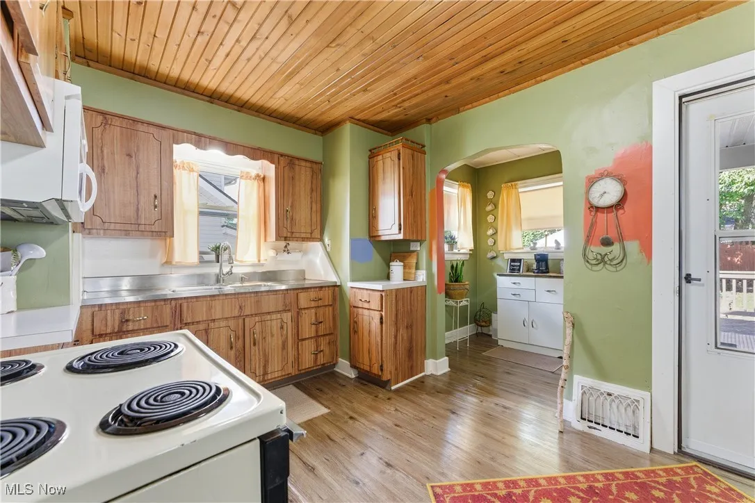 Kitchen featuring brown cabinetry, white appliances, stainless steel counters, light wood-type flooring, and wooden ceiling