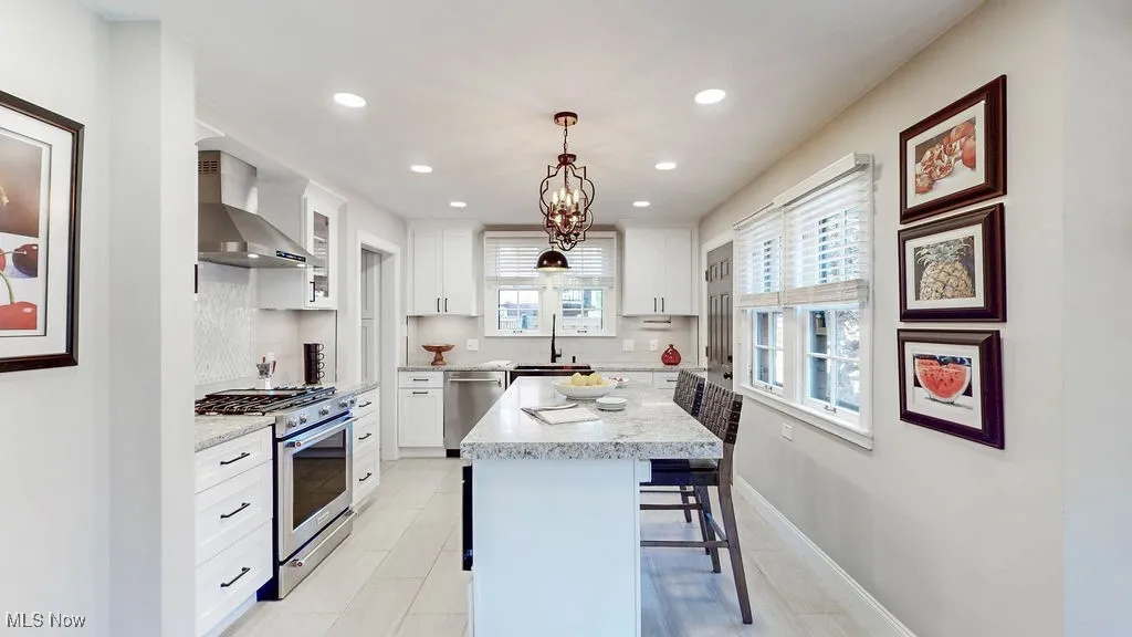 Kitchen with appliances with stainless steel finishes, wall chimney exhaust hood, light tile patterned floors, glass insert cabinets, and white cabinetry