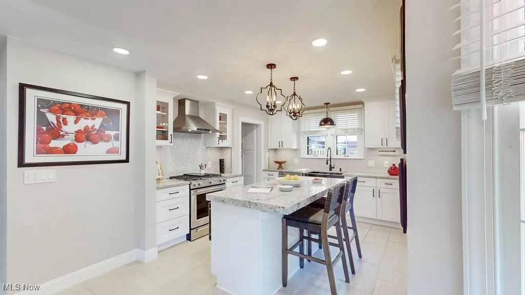 Kitchen featuring a kitchen breakfast bar, high end stainless steel range oven, decorative light fixtures, wall chimney exhaust hood, and glass insert cabinets