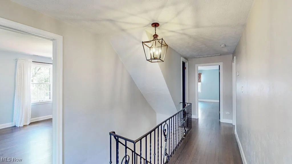 Corridor with an upstairs landing, dark wood-style flooring, a chandelier, and a textured ceiling