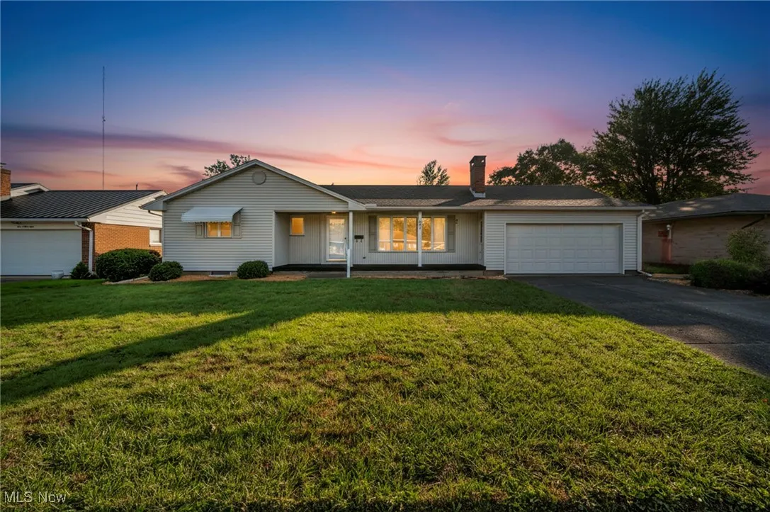 Single story home with a front yard, a chimney, driveway, a garage, and covered porch