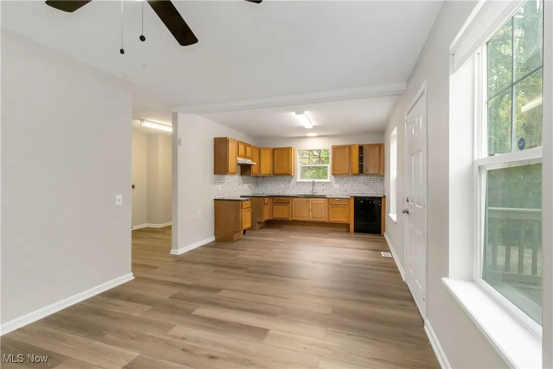 Kitchen with brown cabinets, decorative backsplash, dark wood-style flooring, dishwasher, and a ceiling fan