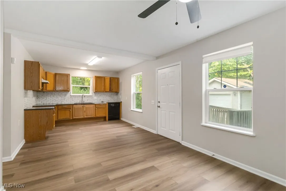 Kitchen with brown cabinetry, decorative backsplash, light wood-style floors, black dishwasher, and dark countertops