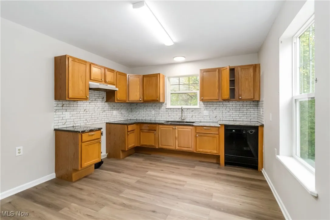 Kitchen featuring decorative backsplash, brown cabinetry, and dishwasher