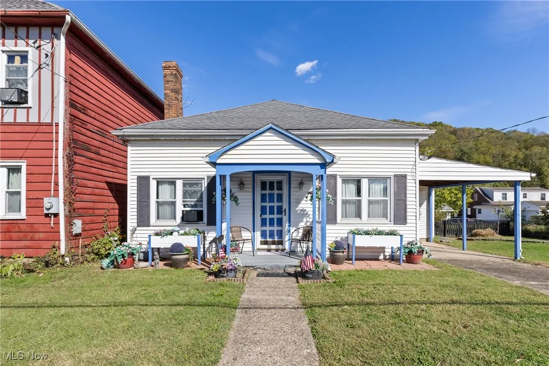 View of front of property featuring a front yard, a shingled roof, an attached carport, a chimney, and covered porch
