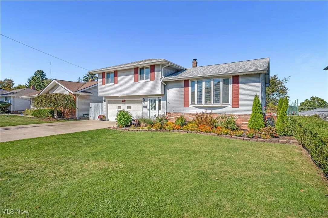Split level home with concrete driveway, a front lawn, a chimney, a garage, and roof with shingles