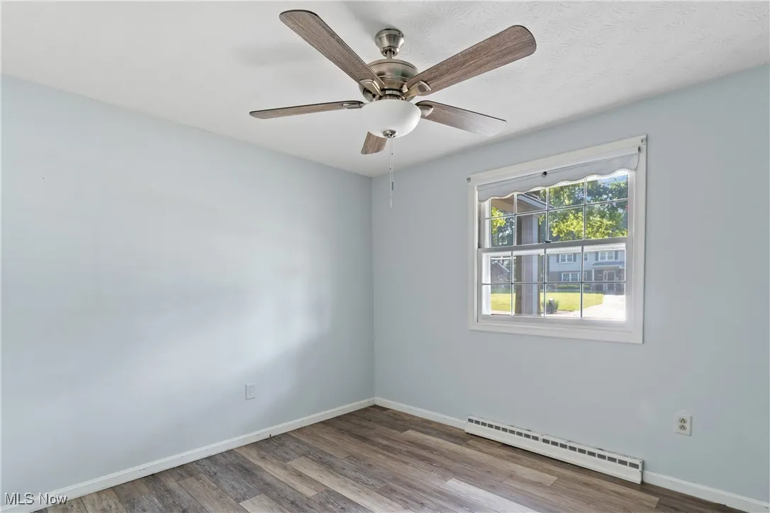 Empty room featuring baseboard heating, wood finished floors, and a ceiling fan