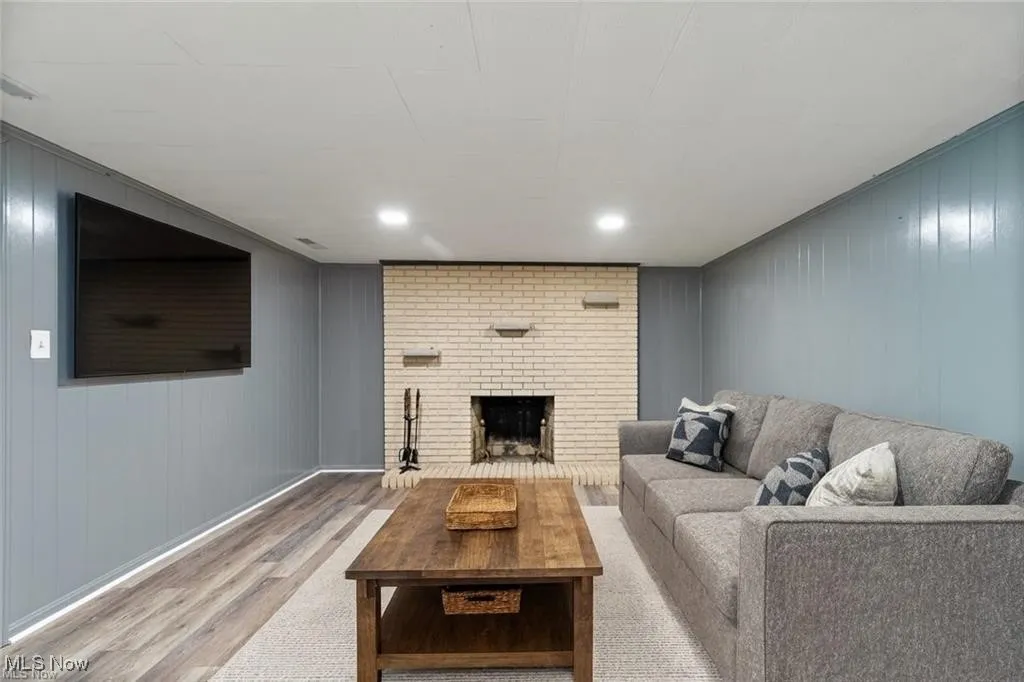 Living area with wood finished floors, wooden walls, a brick fireplace, and recessed​​‌​​​​‌​​‌‌​‌‌​​​‌‌​‌​‌​‌​​​‌​​ lighting