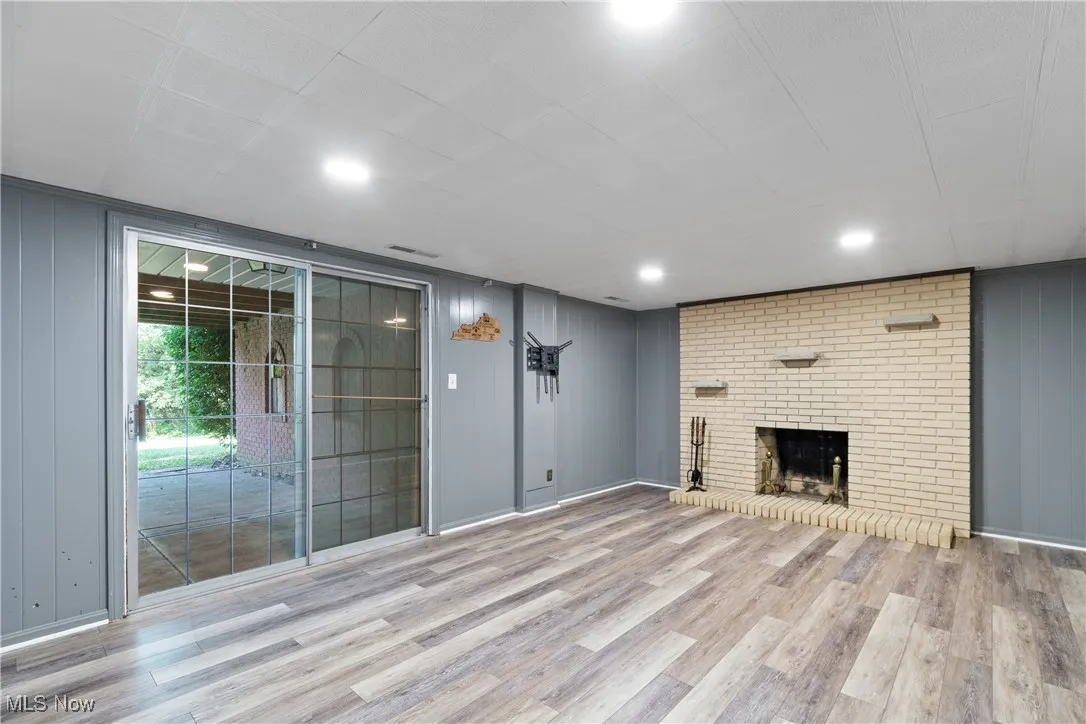 Unfurnished living room featuring a brick fireplace, wood walls, and light wood-type flooring