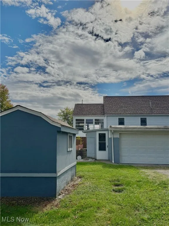 Back of property featuring a shingled roof, a lawn, and driveway
