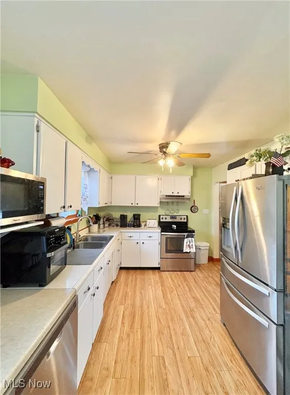 Kitchen with appliances with stainless steel finishes, white cabinetry, light wood-style floors, and light countertops