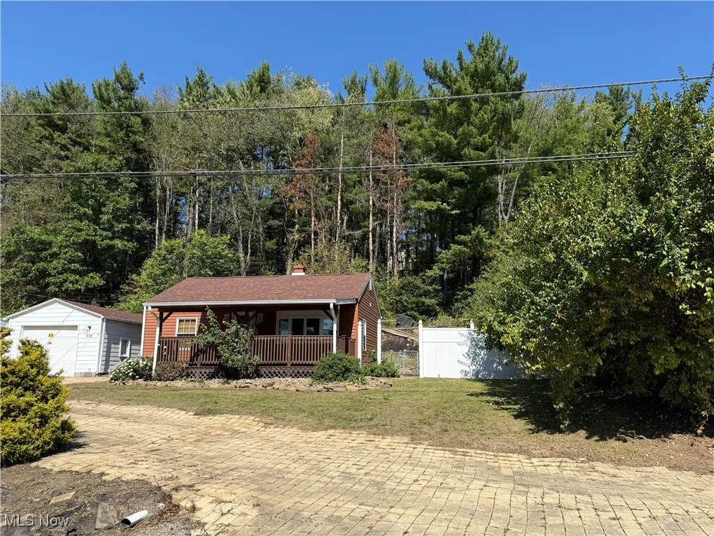 Single story home with covered porch, an outdoor structure, a chimney, a wooded view, and a garage