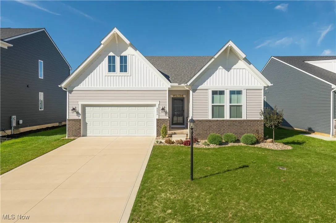 View of front facade with board and batten siding, brick siding, driveway, a garage, and a front lawn