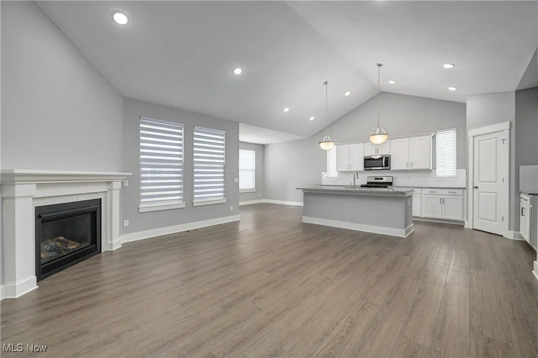 Unfurnished living room featuring dark wood finished floors, plenty of natural light, high vaulted ceiling, a glass covered fireplace, and recessed lighting