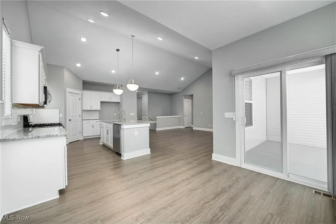 Kitchen with white cabinets, light wood-style floors, lofted ceiling, open floor plan, and light stone countertops