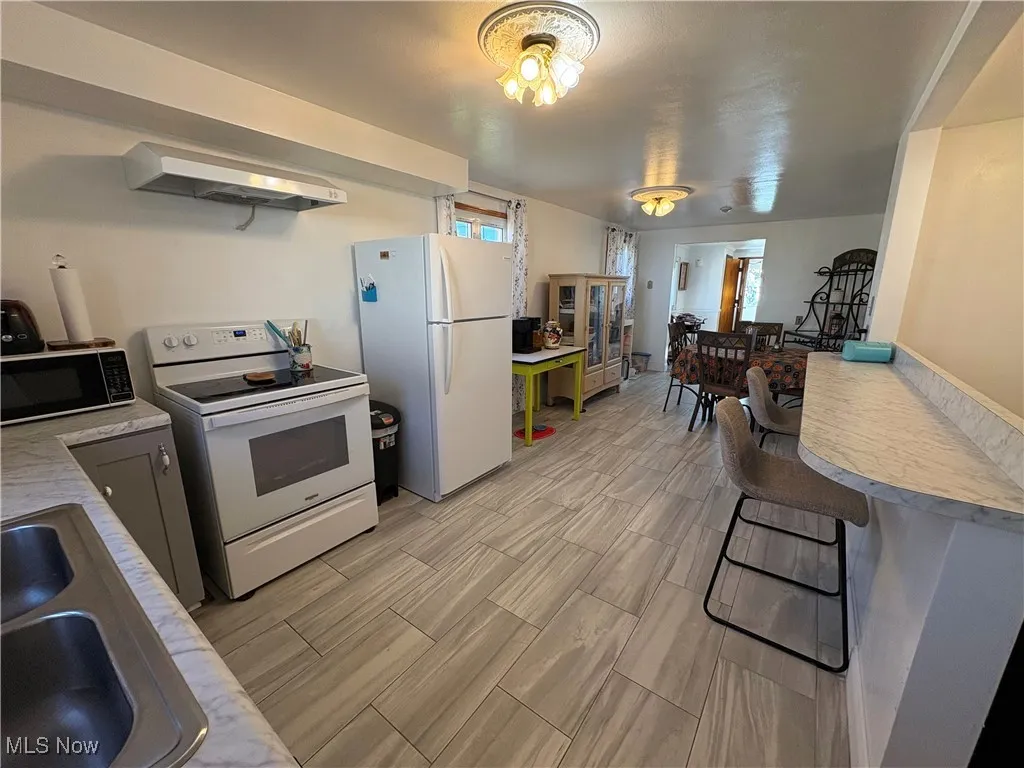 Kitchen with light countertops, appliances, breakfast bar area and ceramic tile floors