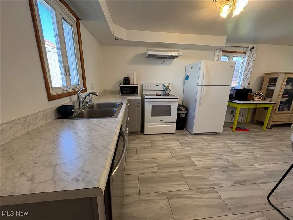 Kitchen with light countertops, appliances, range hood and ceramic tile floors