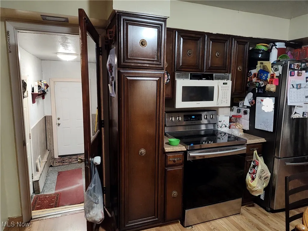 Kitchen featuring dark brown cabinetry, appliances with stainless steel finishes, light wood-type flooring, and light countertops