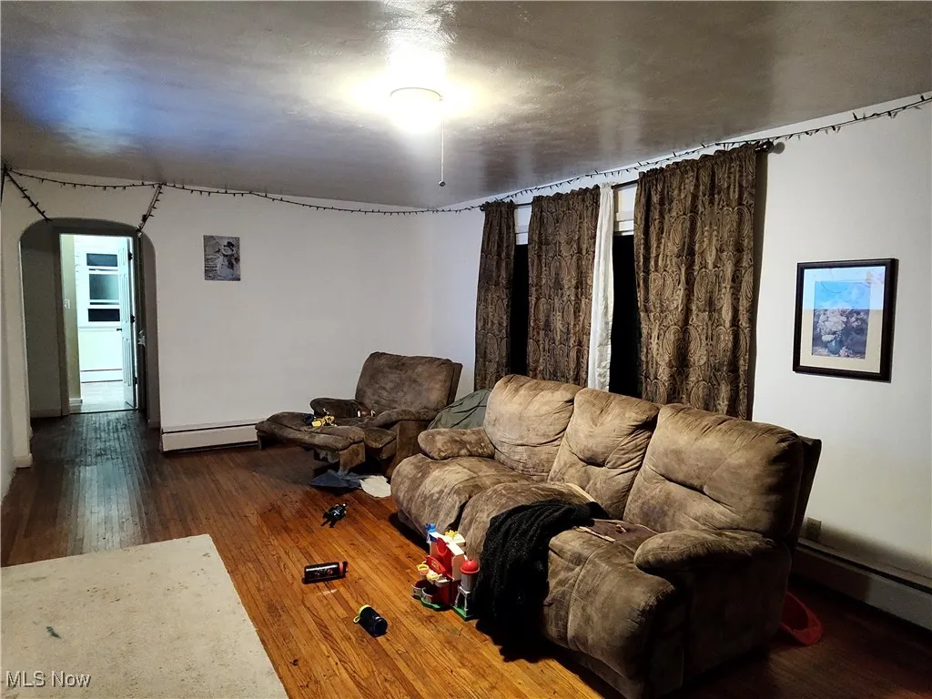 Living area with arched walkways, dark wood-style flooring, and a baseboard heating unit