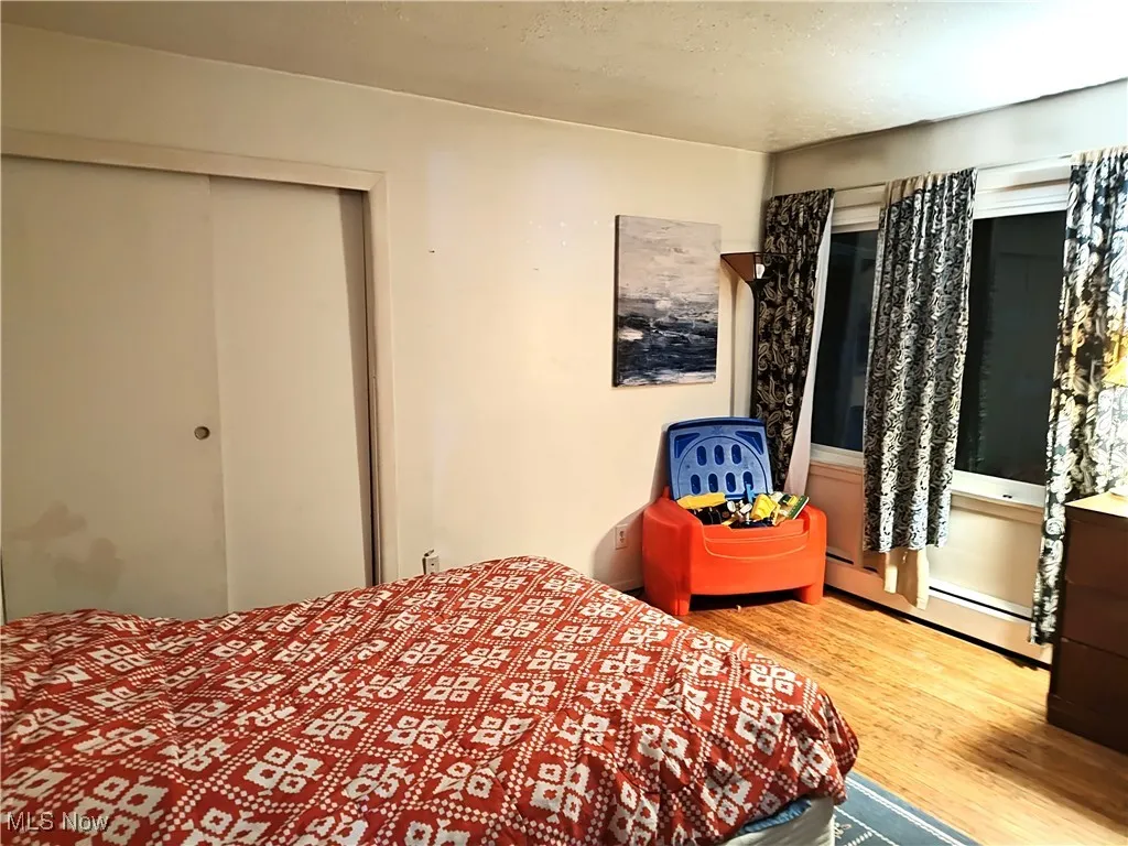 Bedroom featuring wood finished floors, baseboard heating, a closet, and a textured ceiling