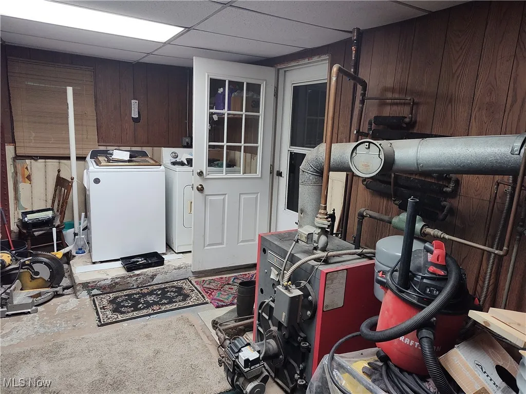 Laundry area with a paneled ceiling, wood walls, and washing machine and dryer