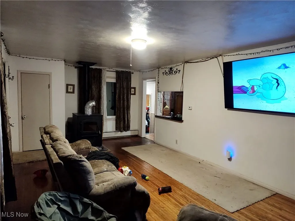 Living area with wood finished floors, a wood stove, and a baseboard heating unit
