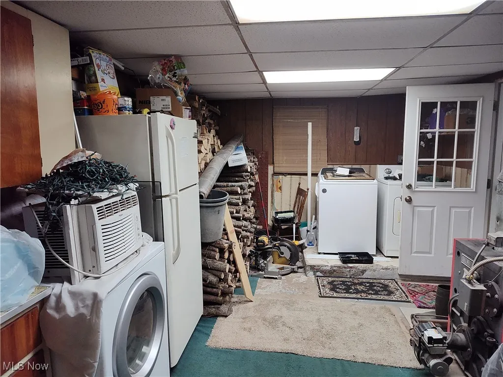 Laundry room featuring a drop ceiling, wood walls, washer and clothes dryer, and concrete flooring