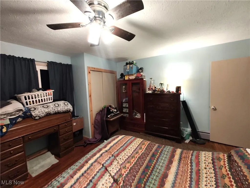 Bedroom featuring a closet, dark wood-style flooring, a textured ceiling, and ceiling fan