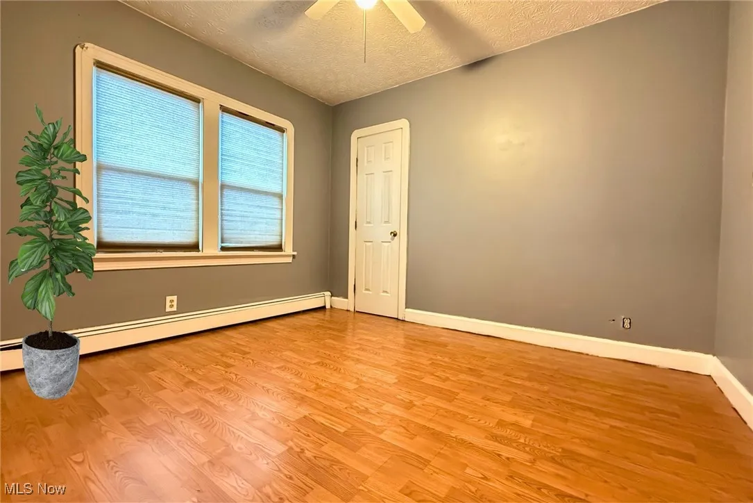 Bedroom (right) featuring a textured ceiling, light wood-style flooring, a baseboard radiator, and a ceiling fan