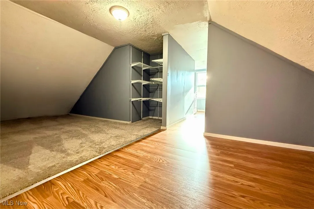 Additional living space featuring a textured ceiling, light wood-style floors, and lofted ceiling