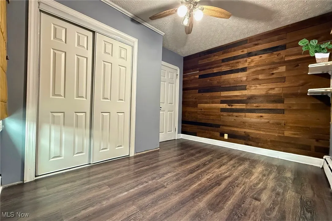 Bedroom (left) featuring a textured ceiling, wood walls, dark wood-style floors, ceiling fan, and a closet