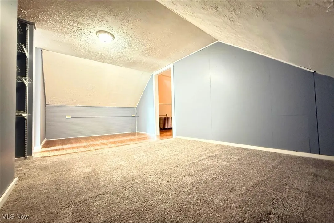Additional living space 2nd fl featuring a textured ceiling, carpet flooring, lofted ceiling, and radiator