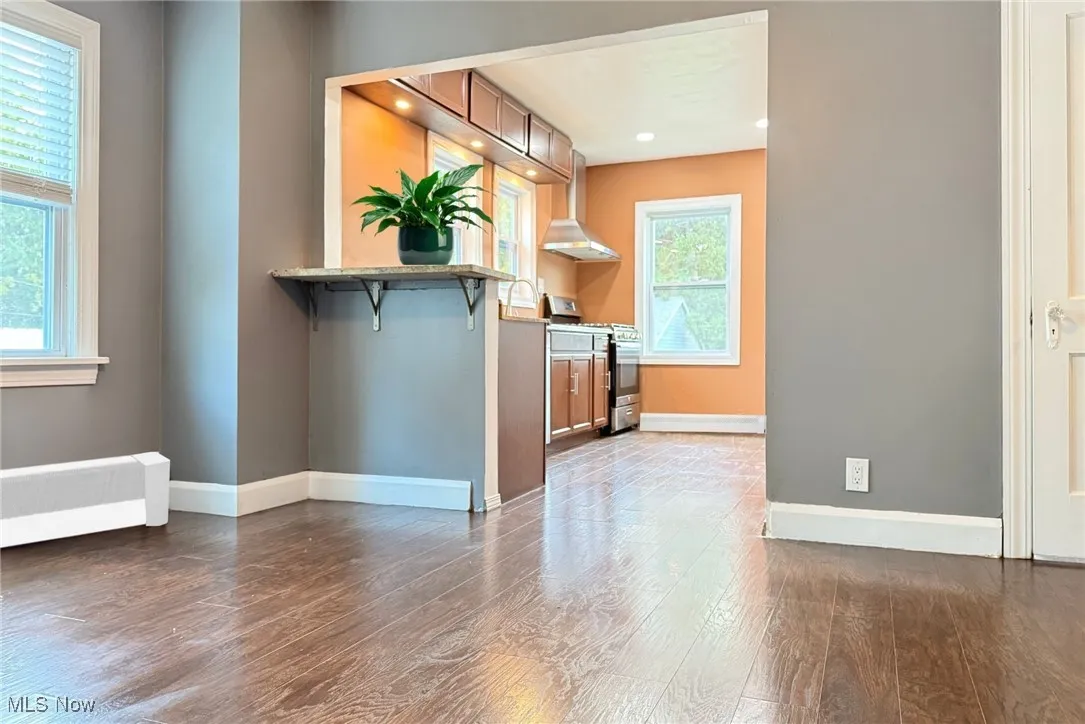 Kitchen featuring stainless steel gas range oven, dark wood-style flooring, wall chimney exhaust hood, a kitchen breakfast bar, and brown cabinets