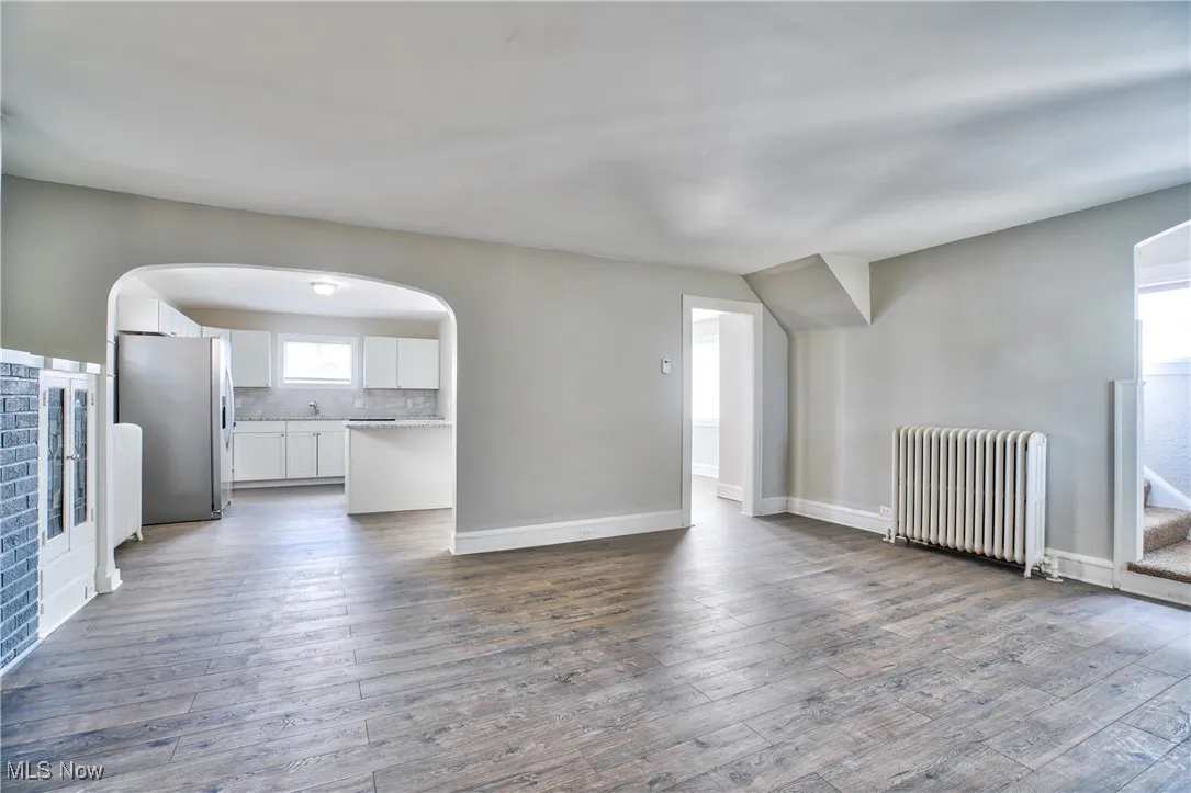 Unfurnished living room with radiator heating unit, arched walkways, and dark wood-style floors