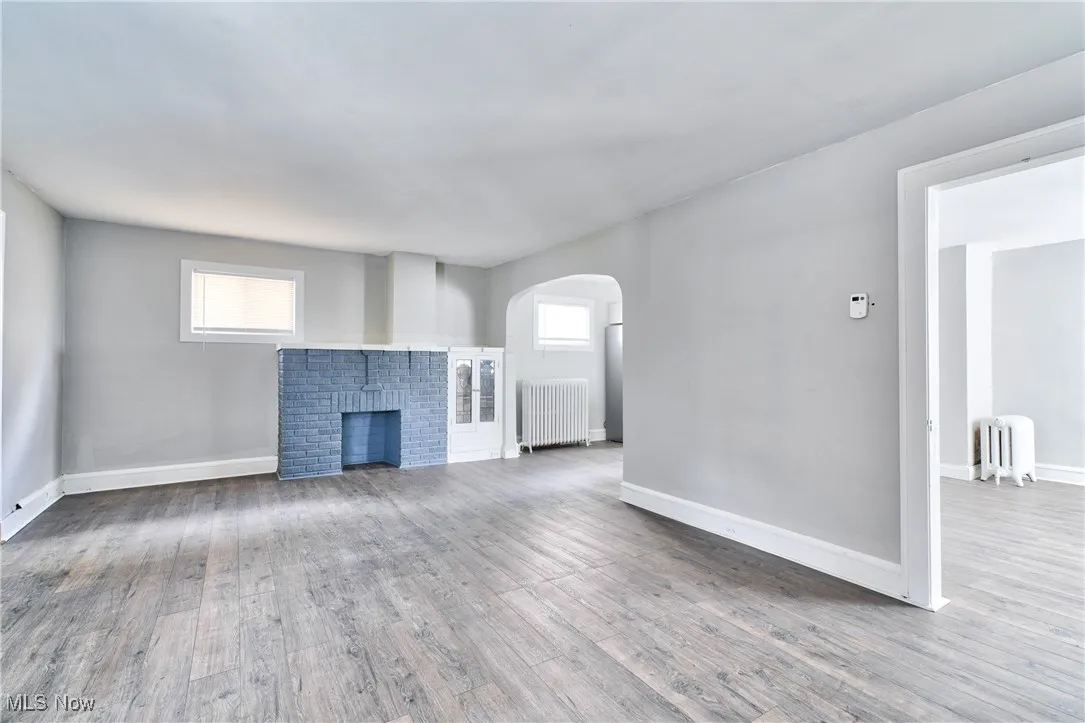 Unfurnished living room with light wood-type flooring, radiator heating unit, a brick fireplace, and arched walkways