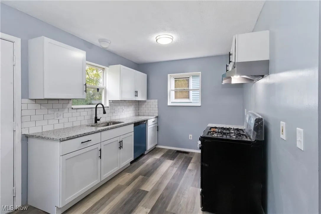 Kitchen with black range with gas cooktop, light stone countertops, white cabinets, dark wood-type flooring, and tasteful backsplash
