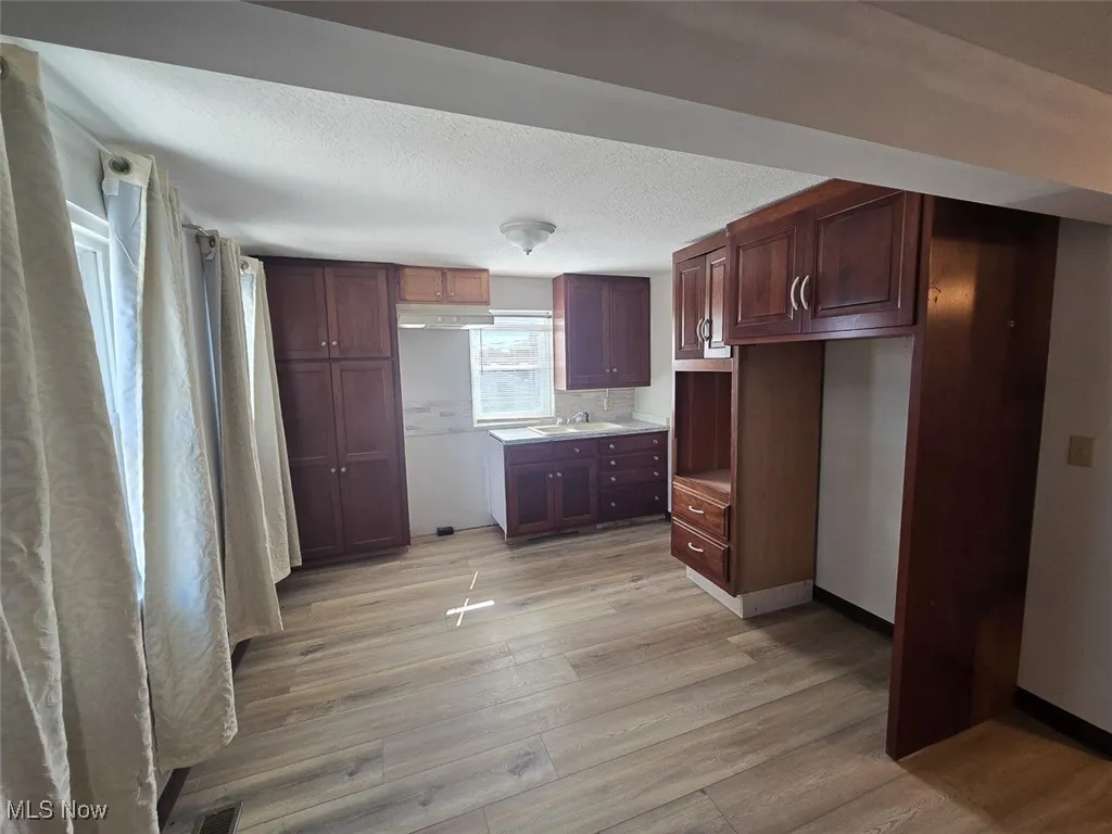 Kitchen with light wood-style floors, a textured ceiling, light countertops, and under cabinet range hood