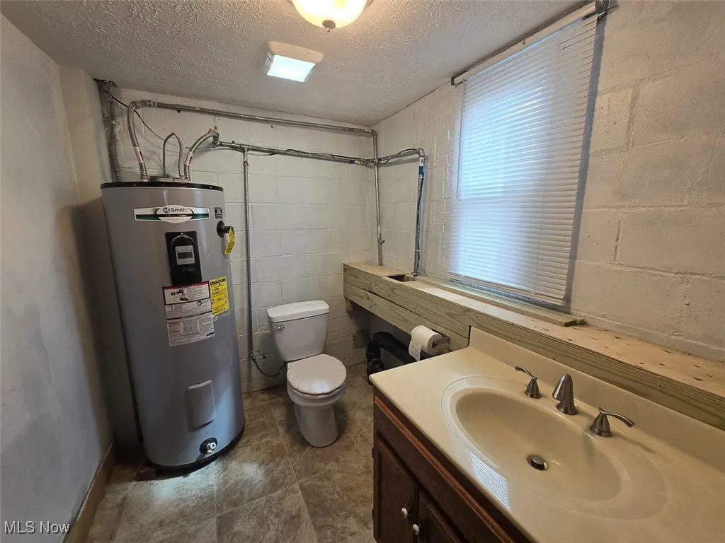 Bathroom with a textured ceiling, electric water heater, vanity, and concrete block wall